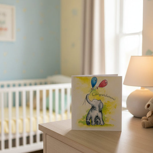 Beautiful congratulations greetings card. The front shows a watercolour-style grey elephant holding blue and red balloons with the word 'Congratulations' written above it.