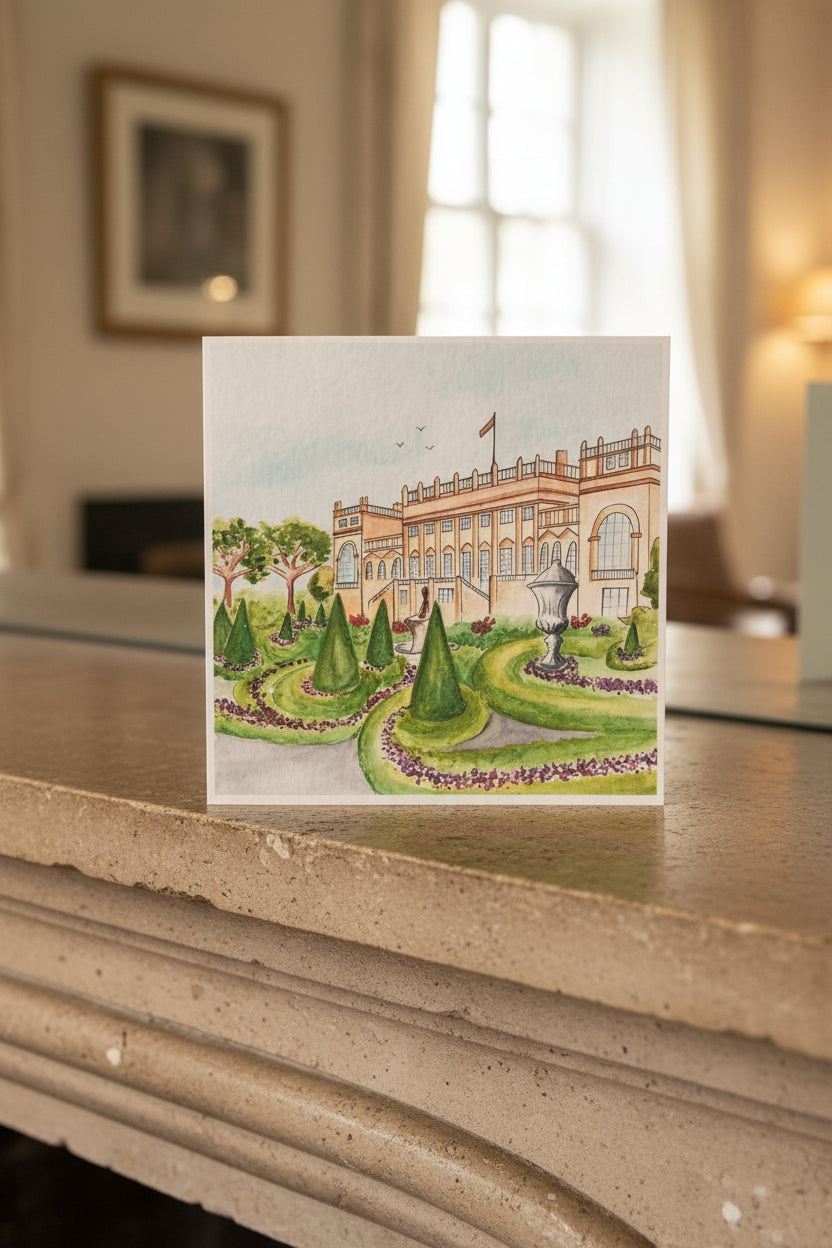 A square watercolor art print depicting a grand classical building with manicured green gardens, shown standing on a white surface against a neutral beige background.